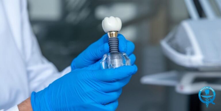 Osoba w niebieskich rękawiczkach trzyma model implantu dentystycznego (korona zęba, łącznik i podstawa) w klinicznym środowisku.