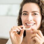 Kobieta trzymająca przezroczysty aparat retencyjny przy ustach, ilustrujący temat retencji po leczeniu ortodontycznym.