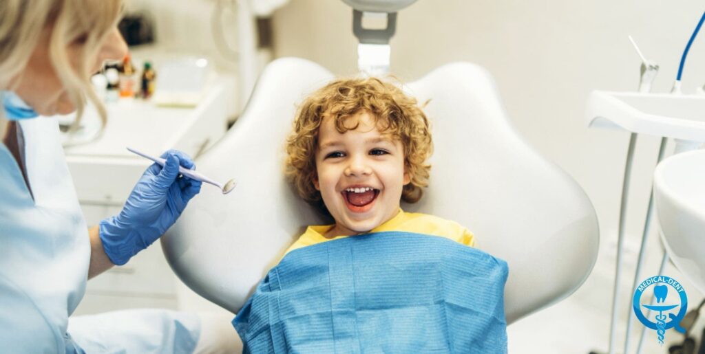 Dziecko na fotelu dentystycznym, dentysta w rękawiczkach trzyma narzędzie do fluoryzacji, dziecko ma uśmiech.