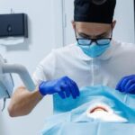 Dentysta w gabinetzie stomatologicznym przeprowadza zabieg chirurgicznego pokrycia odsłoniętych szyjek zębowych pacjenta.