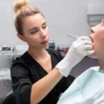 Dentystka w rękawiczkach przeprowadza zabieg wstawiania plomby u pacjentki w gabinecie stomatologicznym.