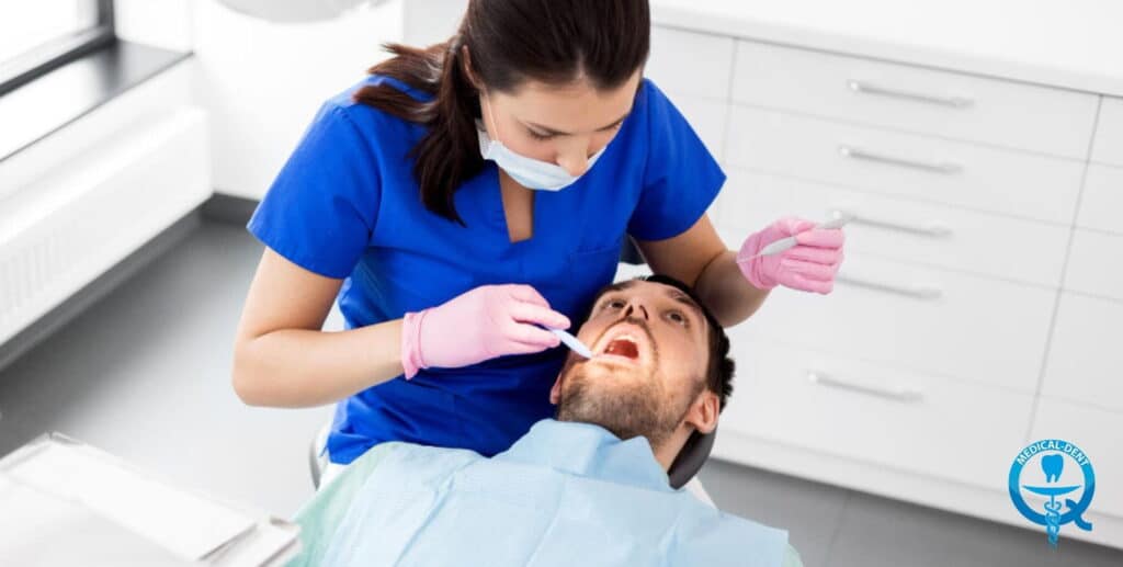 Dentysta w niebieskim stroju i różowych rękawiczkach przeprowadza lakierowanie zębów pacjentowi w klinice dentystycznej w UK.